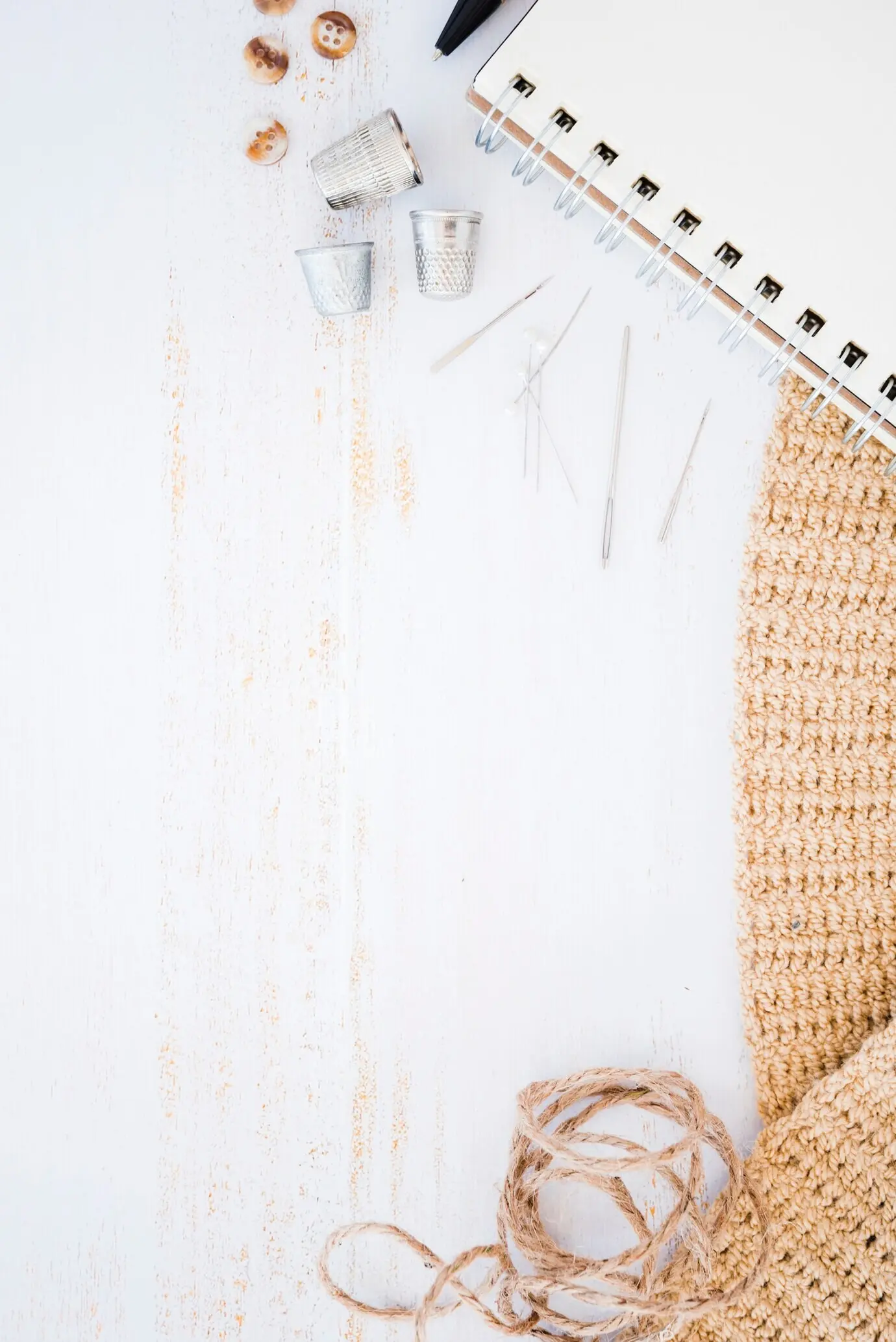 Knopf, Fingerhut, Nadel, Spiralnotizblock, gestrickter Stoff und Schnur auf einem Holztisch.